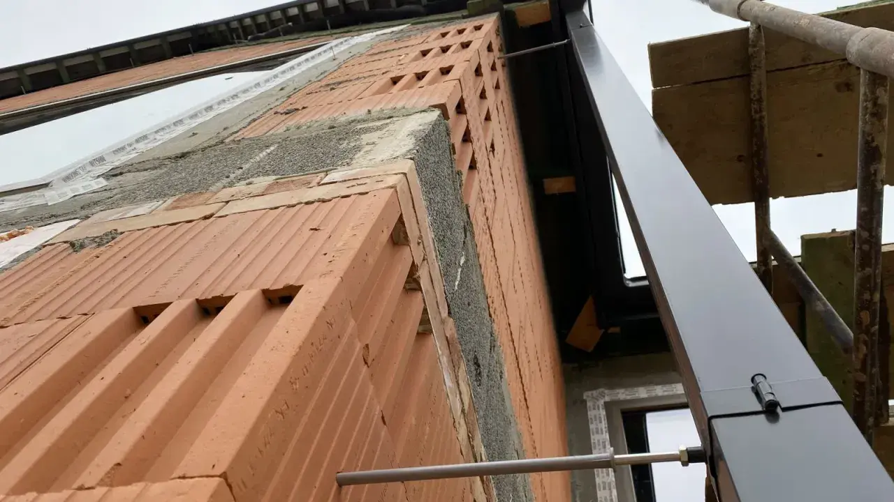 Budowa domu w toku. Widok na ścianę z cegły i rynnę. Trudno ocenić ile rur spustowych na m2 dachu, bo dach jest w budowie.