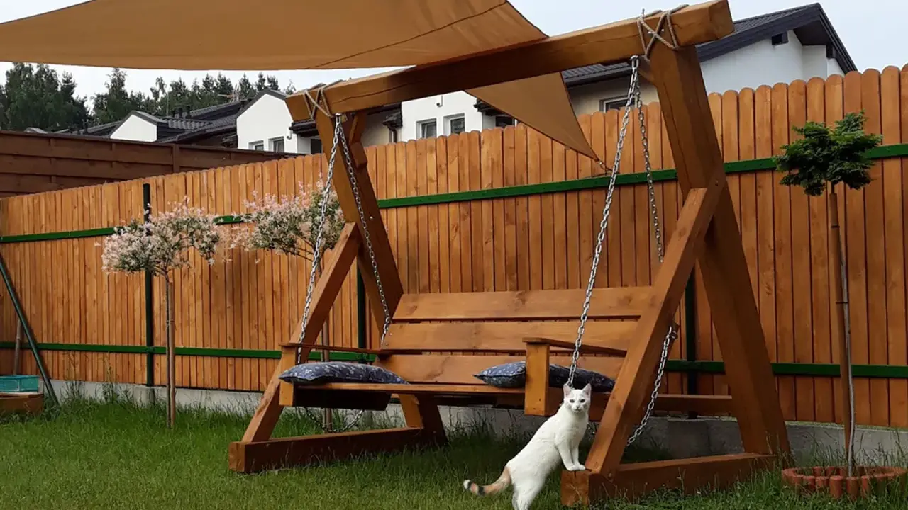 Drewniana huśtawka ogrodowa jak zrobić? Biały kot pilnuje relaksu na łonie natury.