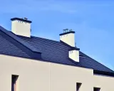 Nowoczesny dach bez okapu konstrukcja z ciemnogranatową dachówką i białymi kominami.