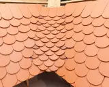 Obróbka kosza lukarny z dachówki ceramicznej. Widok z góry na ułożone dachówki, tworzące łukowaty kształt.