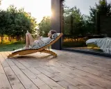 Kobieta relaksuje się na leżaku na tarasie z deski 3 metry, patrząc w telefon. Słońce zachodzi za drzewami.