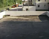 Płaski dach z widocznym odpływem, gotowy na deszcz. W tle budynki i drzewa.