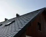Nowy dach z łupka dachowego, montaż zakończony. Widoczne okna dachowe i kominy.