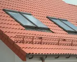 Czerwony dach z dachówkami, oknami dachowymi i rynną. Membrana dachowa w rynnie chroni przed wilgocią.