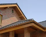 Nowy dom z cegły, widoczna deska czołowa, wysokość okapu i dachówki.