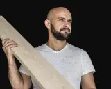 Łysy mężczyzna z brodą trzyma drewnianą deskę, która posłuży jako złącze desek.