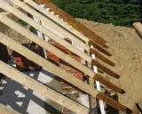 Drewniana konstrukcja dachu, widoczna krokiew narożna zamek, stosy cegieł i piasku.