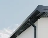 Nowoczesne rynny kwadratowe w kolorze grafitowym odprowadzają wodę z dachu białego domu.
