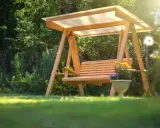 Drewniana huśtawka ogrodowa z wygodnym siedziskiem, otoczona zielenią. Idealne miejsce na relaks, z widocznymi wymiarami siedziska.