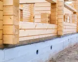 Drewniana konstrukcja domu opiera się na solidnym betonowym fundamencie. Pokazuje to, jak połączyć drewno z betonem w budownictwie.