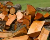 Stos drewna, w tym deska olcha, przygotowana do palenia. Drewno jest pocięte na kawałki o różnej wielkości, z widocznym jasnym rdzeniem i ciemniejszą korą.