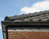 Czarny gont na dachu kopertowym, z rynną i drewnianym podszyciem. Pokazano detale montażu, jak położyć gont na dachu kopertowym.