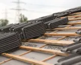 Stosy ciemnych dachówek czekają na montaż na drewnianej konstrukcji dachu.
