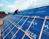 Dach krążynowy w budowie, pracownicy układają niebieską membranę DELTA MAXX na drewnianej konstrukcji.