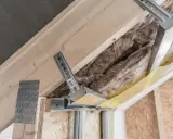 Konstrukcja poddasza z wełną mineralną i profilem metalowym. Widać elementy montażowe, które mogą być używane jako wkręty do wieszaków grzybkowych.