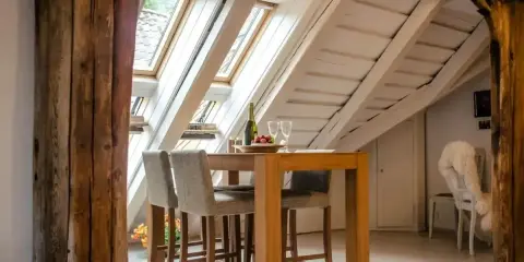 Stare, masywne belki drewniane tworzą ramę dla przytulnego wnętrza ze stołem i hokerami. łączenie belek drewnianych nadaje mu rustykalny charakter.