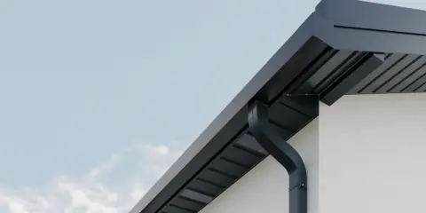 Nowoczesne rynny kwadratowe w kolorze grafitowym odprowadzają wodę z dachu białego domu.