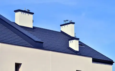 Nowoczesny dach bez okapu konstrukcja z ciemnogranatową dachówką i białymi kominami.