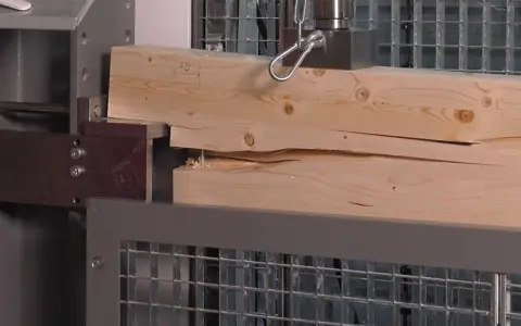 Test wytrzymałości belki drewnianej 10x10. Drewno pęka pod naciskiem maszyny testującej.