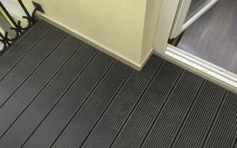 Ciemnoszara deska kompozytowa pełna, tworząca nowoczesną podłogę tarasu, z widocznym fragmentem drzwi balkonowych i jasną ścianą.