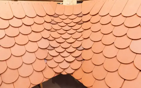 Obróbka kosza lukarny z dachówki ceramicznej. Widok z góry na ułożone dachówki, tworzące łukowaty kształt.