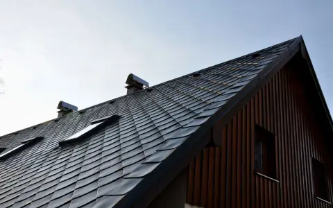Nowy dach z łupka dachowego, montaż zakończony. Widoczne okna dachowe i kominy.