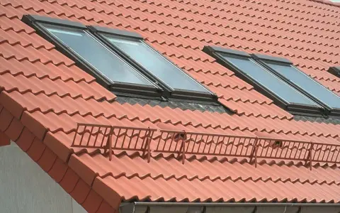 Czerwony dach z dachówkami, oknami dachowymi i rynną. Membrana dachowa w rynnie chroni przed wilgocią.