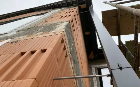 Budowa domu w toku. Widok na ścianę z cegły i rynnę. Trudno ocenić ile rur spustowych na m2 dachu, bo dach jest w budowie.
