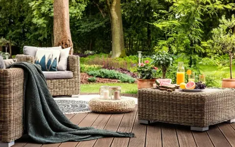 Relaks na tarasie z meblami z plecionki, przypominającej naturalne **drewno egzotyczne**. Na stoliku owoce i napoje, obok wygodna sofa.