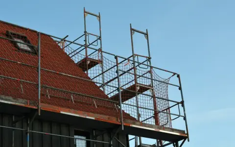 Metalowe rusztowanie na dachu z czerwonej dachówki, gotowe do prac remontowych.