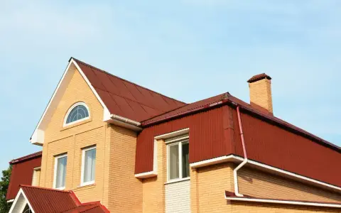 Dach mansardowy konstrukcja z czerwonej blachy falistej, z ceglaną ścianą i kominem.