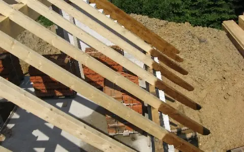 Drewniana konstrukcja dachu, widoczna krokiew narożna zamek, stosy cegieł i piasku.