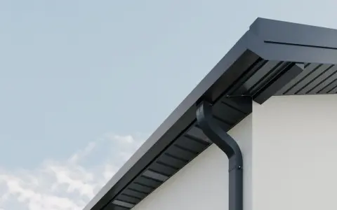 Nowoczesne rynny kwadratowe w kolorze grafitowym odprowadzają wodę z dachu białego domu.