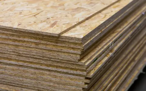 Stos płyt OSB, idealnych jako podkład pod pokrycie dachowe. Zastanawiasz się, czym pokryć dach z płyty OSB? Oto materiał, który Ci w tym pomoże.