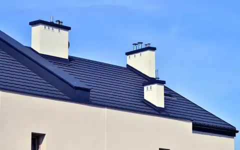 Nowoczesny dom z ciemnym dachem i kominami. Dyskretna rynna ukryta w elewacji zapewnia estetykę.