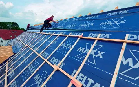 Dach krążynowy w budowie, pracownicy układają niebieską membranę DELTA MAXX na drewnianej konstrukcji.