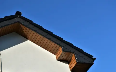 Elegancka podbitka z płyty OSB pod ciemnym dachem, kontrastująca z jasną elewacją i błękitem nieba.