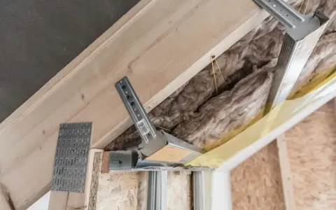Konstrukcja poddasza z wełną mineralną i profilem metalowym. Widać elementy montażowe, które mogą być używane jako wkręty do wieszaków grzybkowych.
