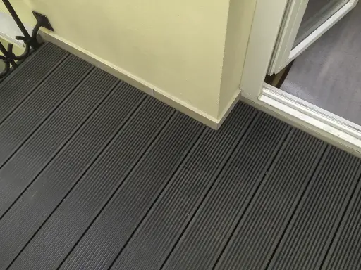 Ciemnoszara deska kompozytowa pełna, tworząca nowoczesną podłogę tarasu, z widocznym fragmentem drzwi balkonowych i jasną ścianą.