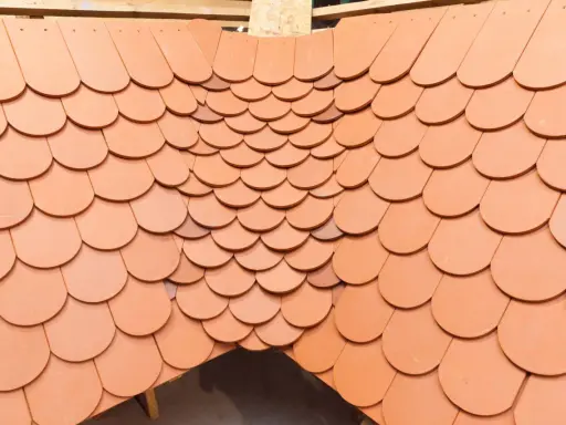 Obróbka kosza lukarny z dachówki ceramicznej. Widok z góry na ułożone dachówki, tworzące łukowaty kształt.