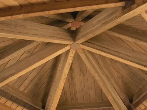 Drewniana konstrukcja dachu z widocznymi belkami i okapem. Ozdoba szczytu dachu to centralny, wieloboczny element łączący.