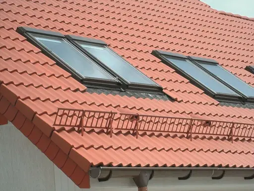 Czerwony dach z dachówkami, oknami dachowymi i rynną. Membrana dachowa w rynnie chroni przed wilgocią.