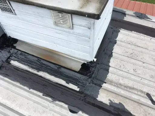 Uszczelnianie dachu, gdzie dach przecieka na wkrętach. Czarna masa izolacyjna na białej blasze.