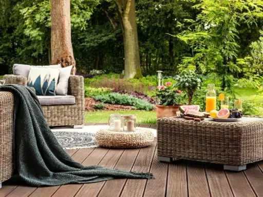 Relaks na tarasie z meblami z plecionki, przypominającej naturalne **drewno egzotyczne**. Na stoliku owoce i napoje, obok wygodna sofa.