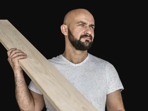 Łysy mężczyzna z brodą trzyma drewnianą deskę, która posłuży jako złącze desek.