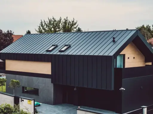 Nowoczesny dom z ciemną elewacją z blachy trapezowej, drewnianymi panelami i dwoma oknami dachowymi.