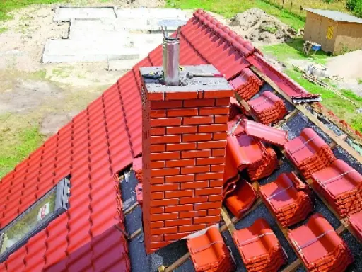 Obróbka komina okrągłego blachą trapezową na czerwonym dachu. Dachówka w paczkach czeka na ułożenie.