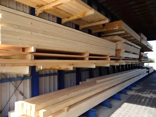 Stosy drewna KVH na regałach. Długie, jasne belki ułożone warstwowo, gotowe do dalszego wykorzystania.