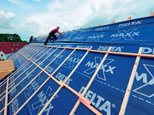 Dach krążynowy w budowie, pracownicy układają niebieską membranę DELTA MAXX na drewnianej konstrukcji.