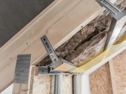 Konstrukcja poddasza z wełną mineralną i profilem metalowym. Widać elementy montażowe, które mogą być używane jako wkręty do wieszaków grzybkowych.